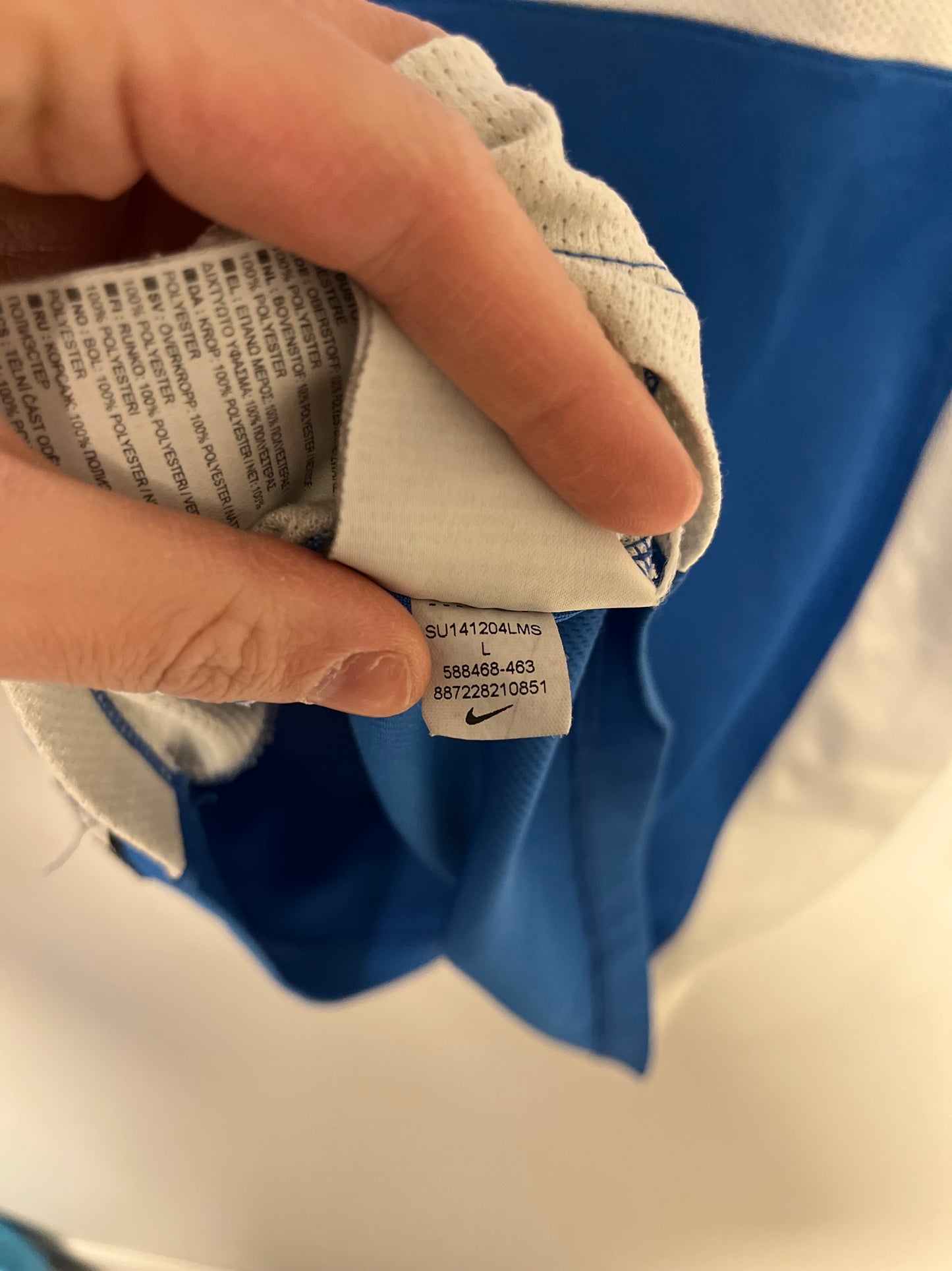 Hand holding a white sneaker with a visible Nike tag against a blue and white background