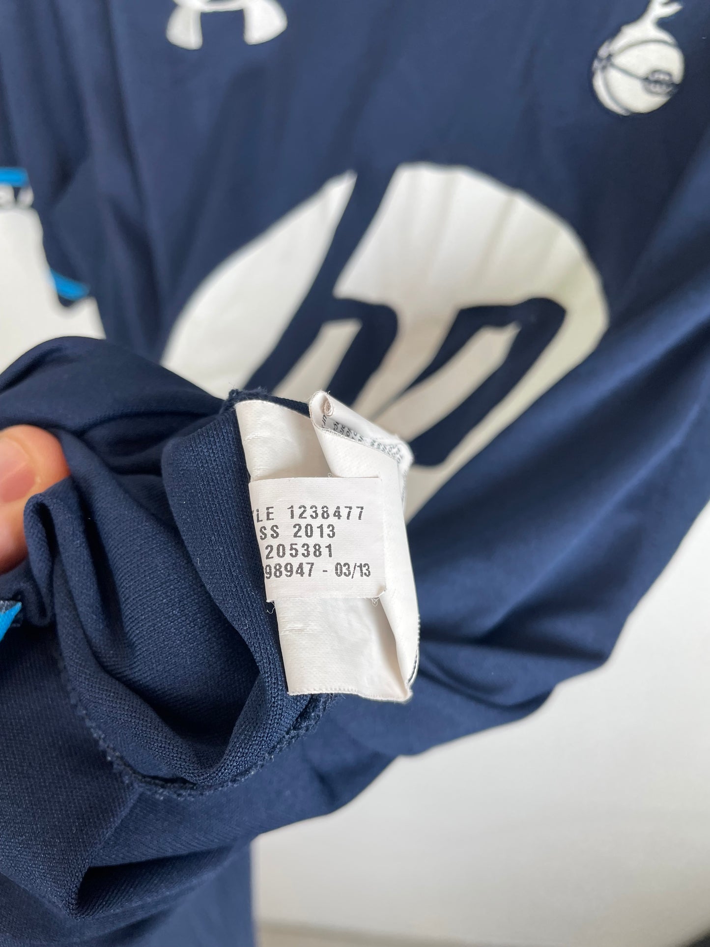 Close-up of a navy blue athletic jersey with a white graphic print, showing the inner size tag held by a hand.