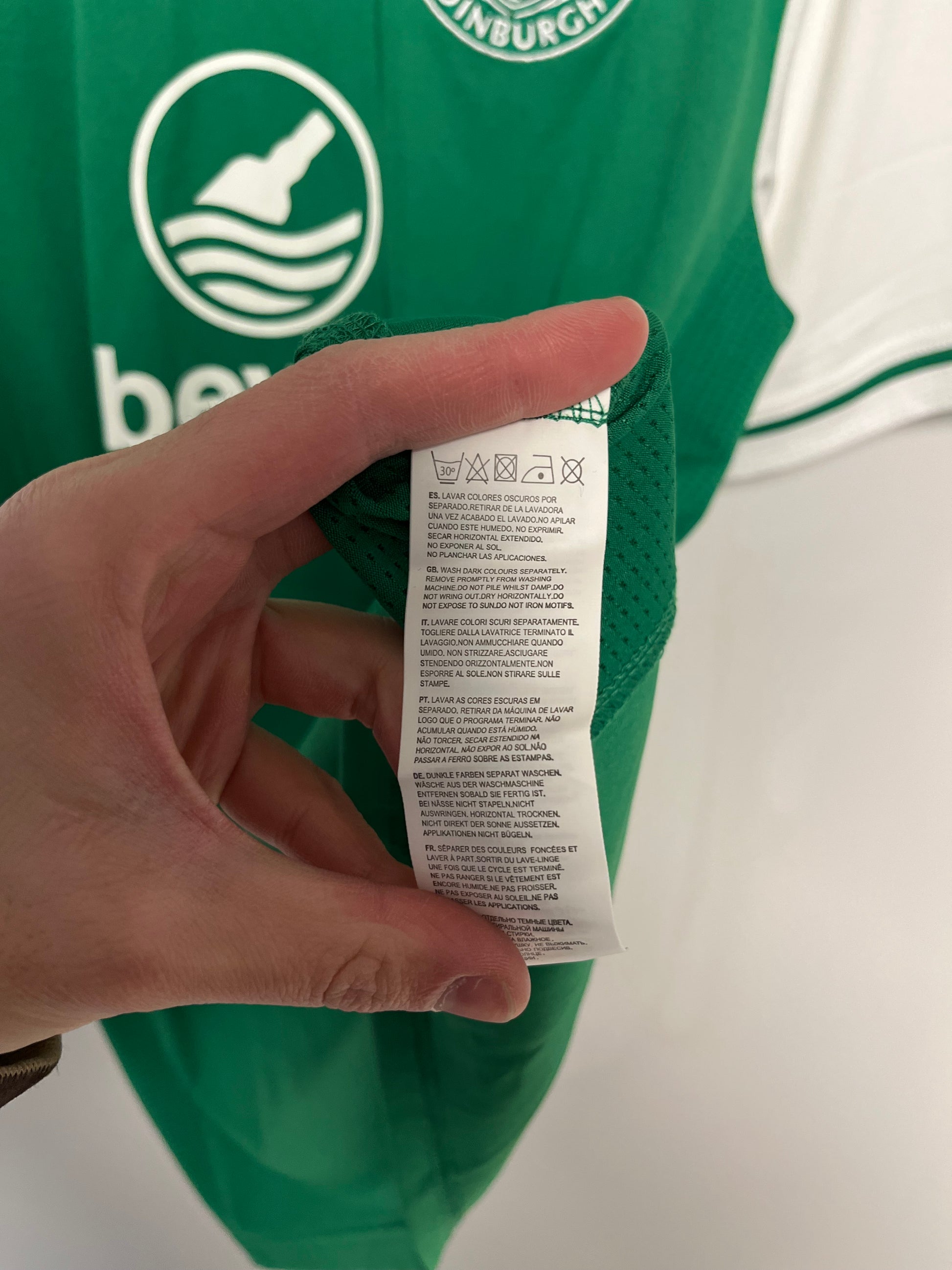 Hand holding a label in front of a green garment with a logo
