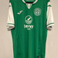 Green Hibernian jersey with white accents on a hanger against a beige background