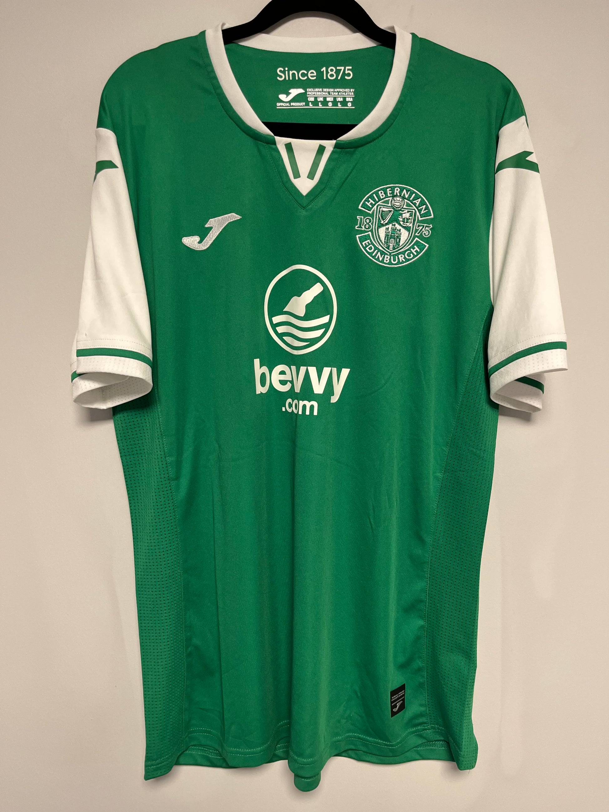 Green Hibernian jersey with white accents on a hanger against a beige background
