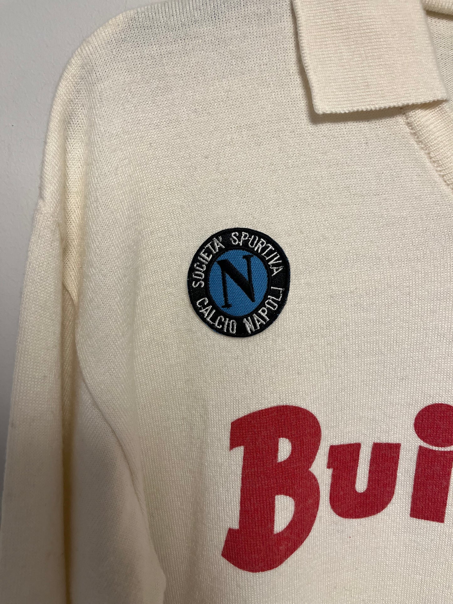 Close-up of a beige napoli shirt with a logo and text on a gray background