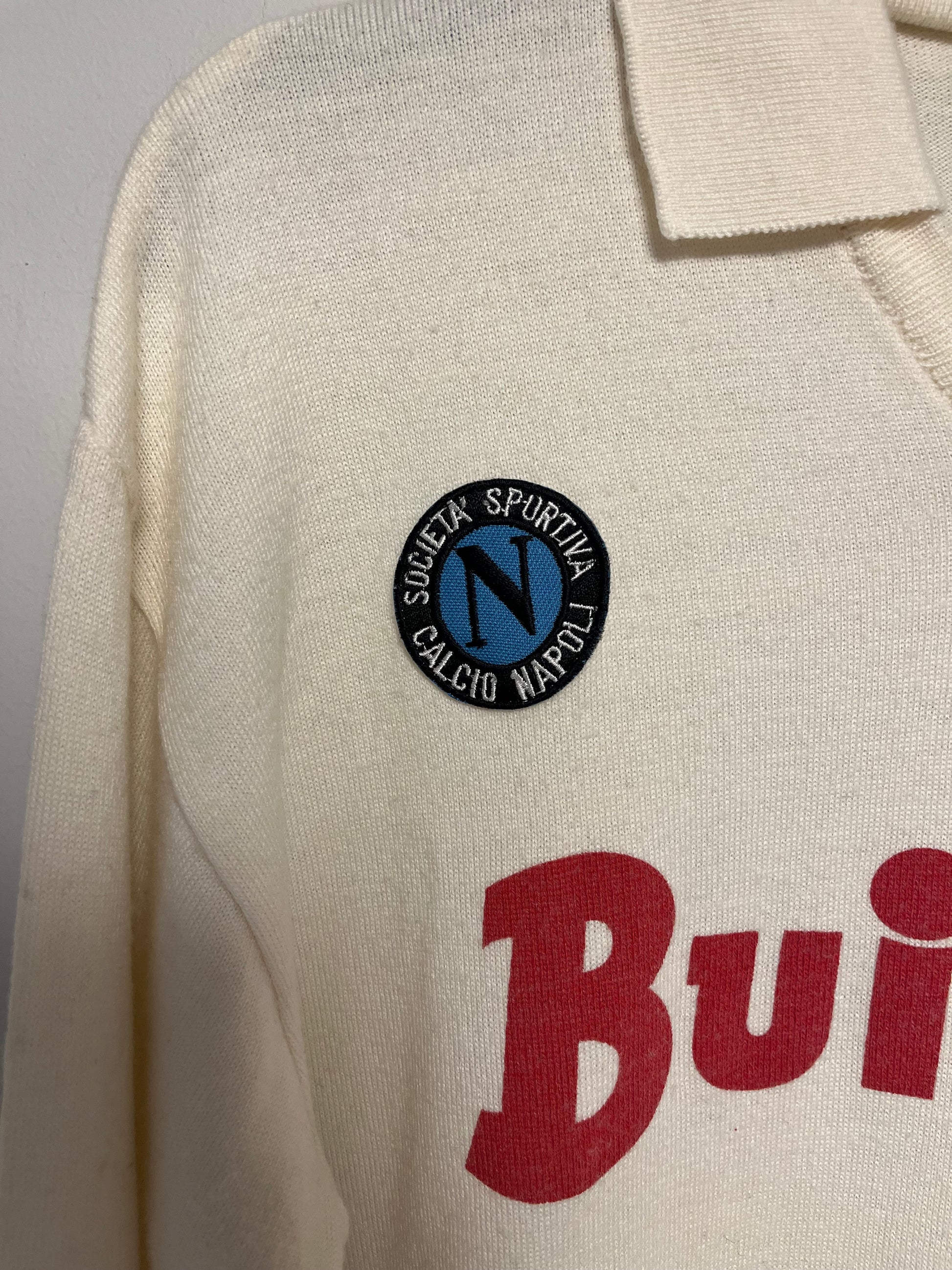 Close-up of a beige napoli shirt with a logo and text on a gray background