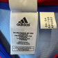 Close-up of an Adidas garment interior label with the Adidas logo and size/lot information, shown against blue and red mesh fabric.