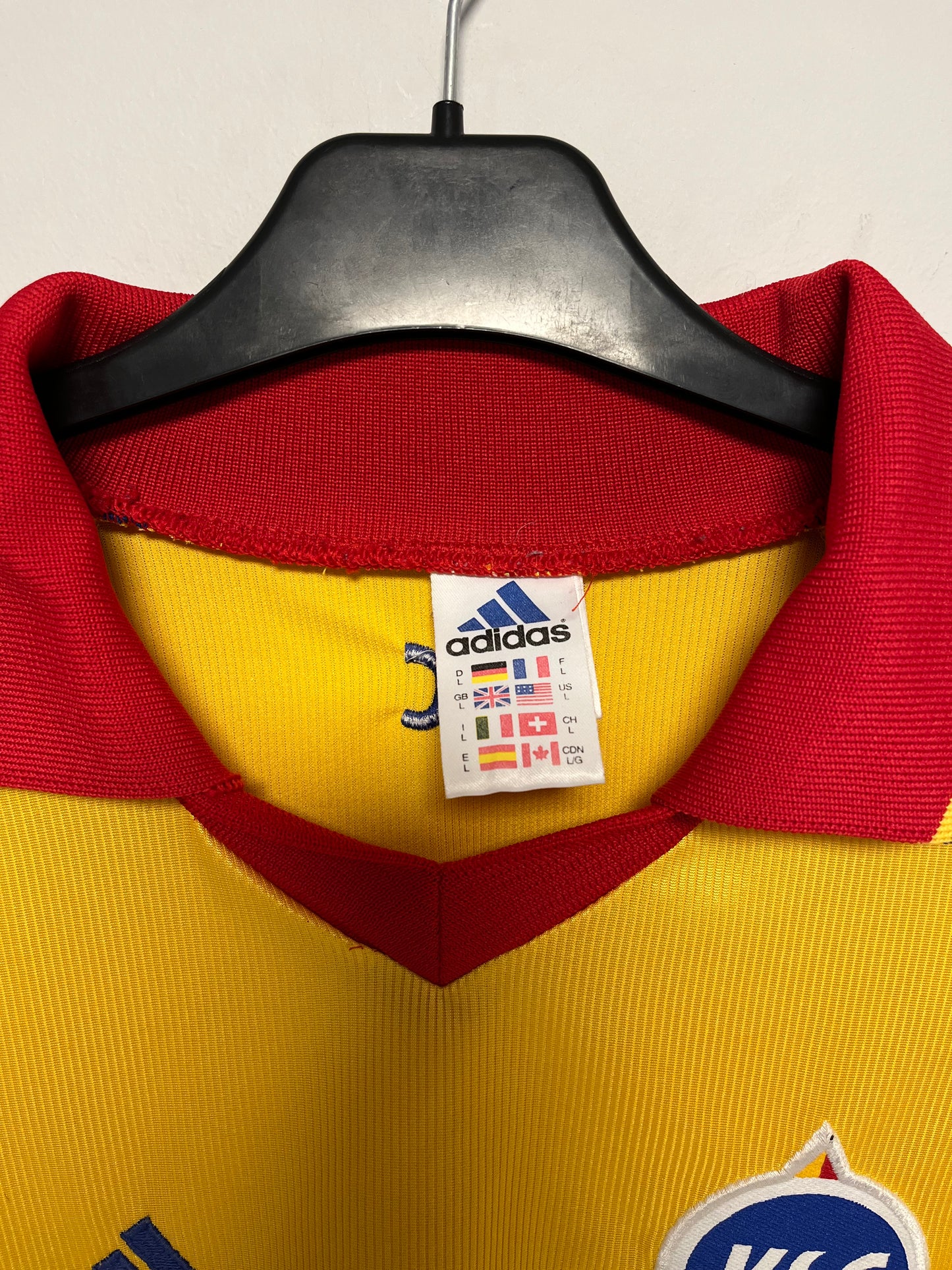 Yellow sports jersey with red collar on a hanger, featuring Adidas logo.