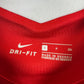 Close-up of a red athletic jersey showing the white Nike swoosh and DRI-FIT text inside the collar, along with size information.