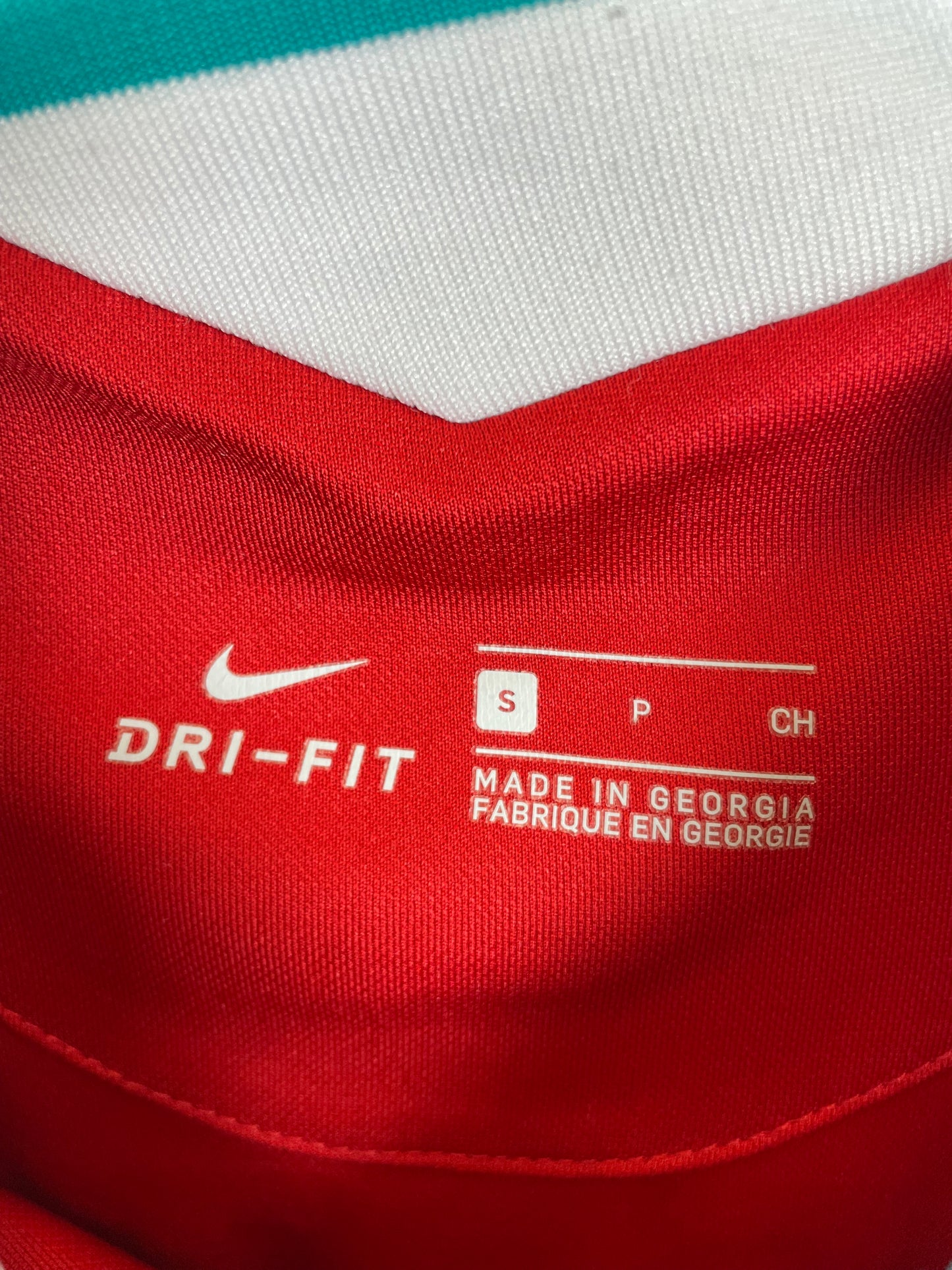Close-up of a red athletic jersey showing the white Nike swoosh and DRI-FIT text inside the collar, along with size information.