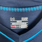Close-up of the inside collar of a navy blue Under Armour athletic top, showing the inner label with 'SWEAT' and 'REGULAR' text, plus a light blue houndstooth pattern along the inner neckline.