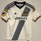 White LA Galaxy Home Shirt 15/16 Gerrard Kids | MLS  jersey with black and yellow accents, featuring Adidas logo and Herbalife branding, on a gray background.
