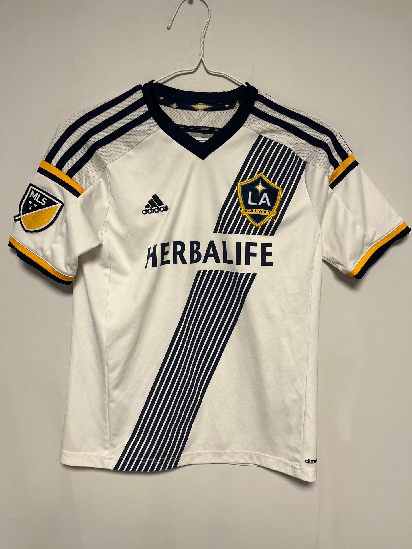 White LA Galaxy Home Shirt 15/16 Gerrard Kids | MLS  jersey with black and yellow accents, featuring Adidas logo and Herbalife branding, on a gray background.