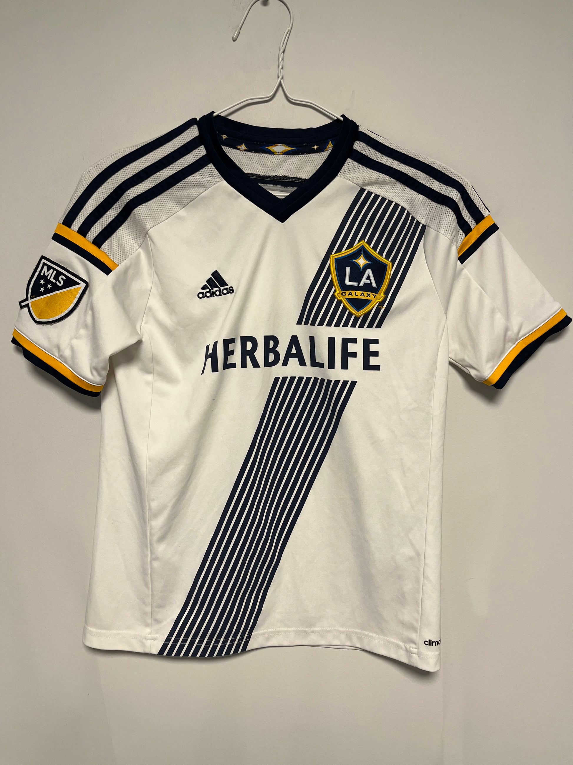 White LA Galaxy Home Shirt 15/16 Gerrard Kids | MLS  jersey with black and yellow accents, featuring Adidas logo and Herbalife branding, on a gray background.