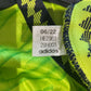 Close-up of a neon green footballdrakter dame outfit with an Adidas tag showing date code and product details.
