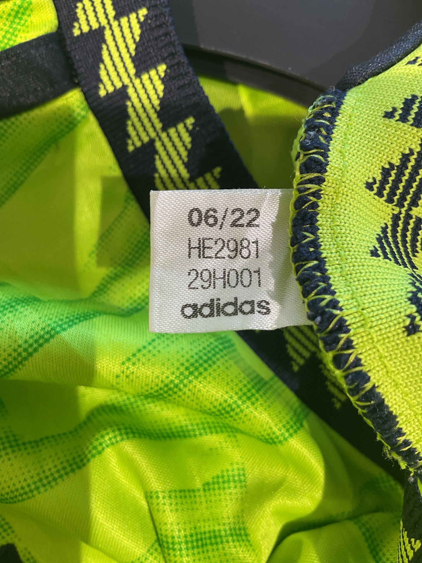 Close-up of a neon green footballdrakter dame outfit with an Adidas tag showing date code and product details.