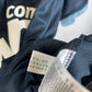 Close-up of a dark navy blue garment tag with printed size and care instructions, attached to a dark navy mesh fabric garment.