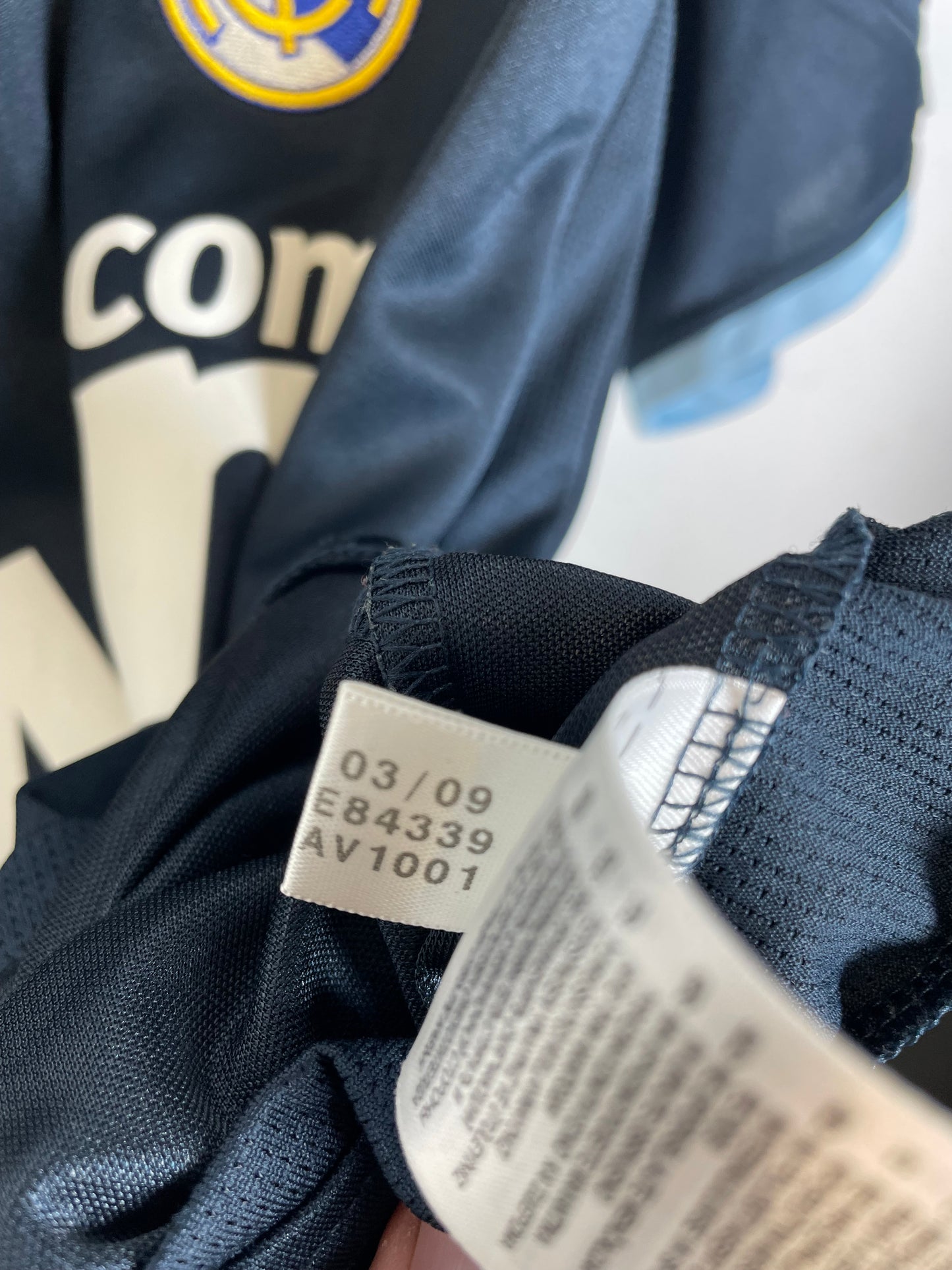 Close-up of a dark navy blue garment tag with printed size and care instructions, attached to a dark navy mesh fabric garment.