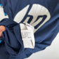 Close-up of a navy blue athletic jersey with a white graphic print, showing the inner size tag held by a hand.