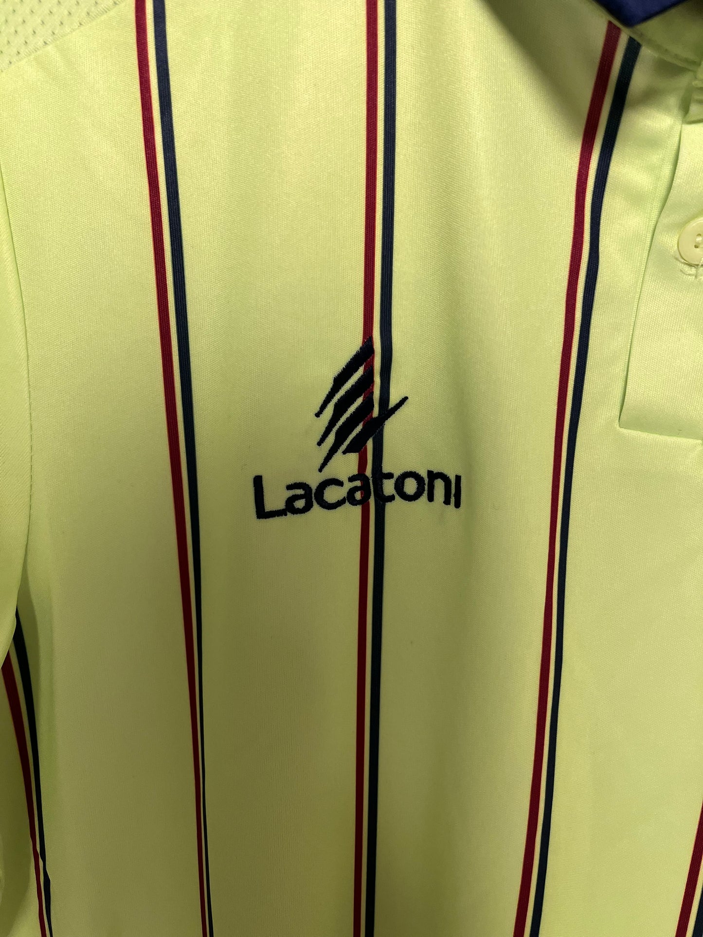 Close-up of a cream-colored shirt with red and blue stripes and 'Lacoste football shirt' branding.