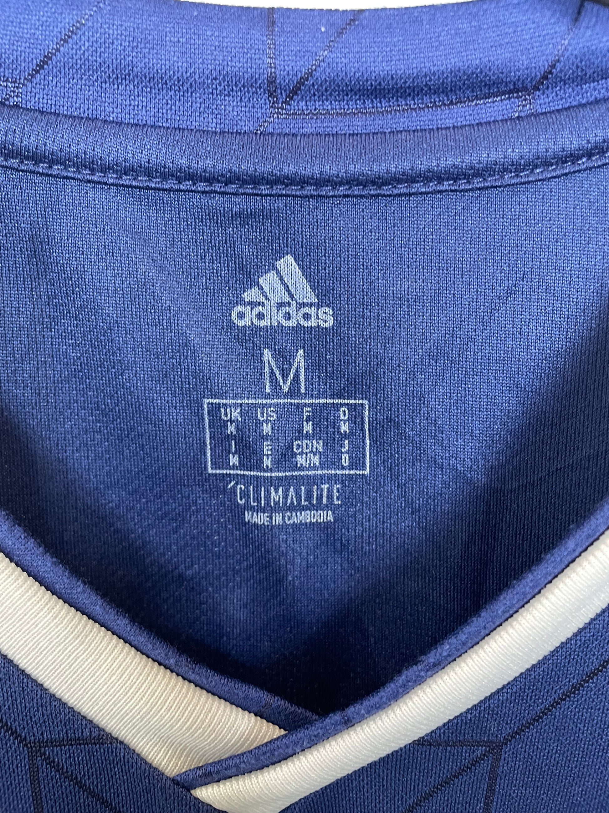 Close-up of a blue Adidas football shirt with branding and text.