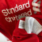 Close-up of a red sports jersey with white 'Standard Chartered' text and a white care tag attached near the collar.
