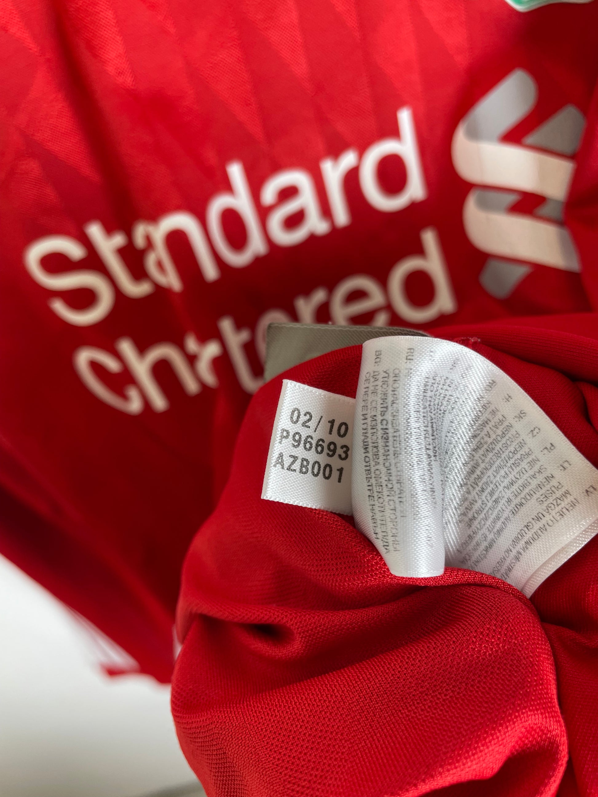 Close-up of a red sports jersey with white 'Standard Chartered' text and a white care tag attached near the collar.