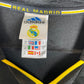 Close-up of the interior label of a black Adidas Real Madrid bag, showing the brand logo, team crest, and size information, with yellow accents and the text 'REAL MADRID' on the side.