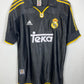 A black Real Madrid soccer jersey with yellow trim and white logos, laid flat on a light gray background.